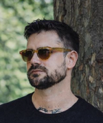 Porträt eines Mannes mit Bart und Sonnenbrille vor einem Baum