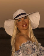 Porträt einer lächelnden blonden Frau mit Sonnenhut und Sommerkleid im Abendlicht