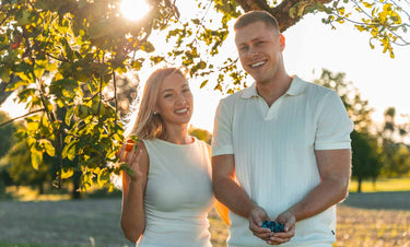Die Elixsír-Gründer Viktoria und Adrian lächeln im Gegenlicht in einem Obstgarten und halten Heidelbeeren in den Händen