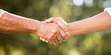Zwei Personen geben sich die Hand vor grün verschwommenem Hintergrund